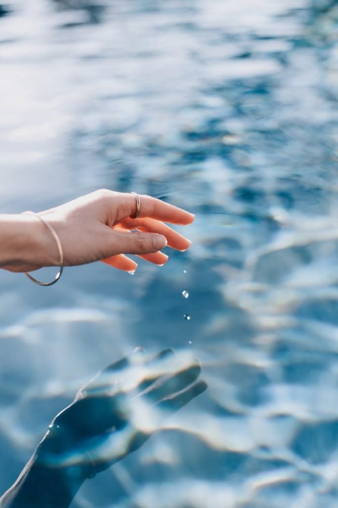 A womans hand gently touches the clear blue water surface creating serene ripples.