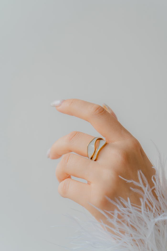 Close-up of a womans hand wearing a stylish gold ring with a feathered sleeve background.