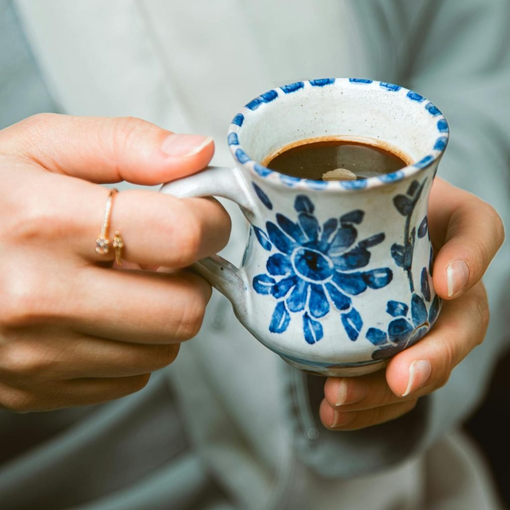 Close-up of a hand holding a ceramic mug with traditional Turkish coffee, floral design.