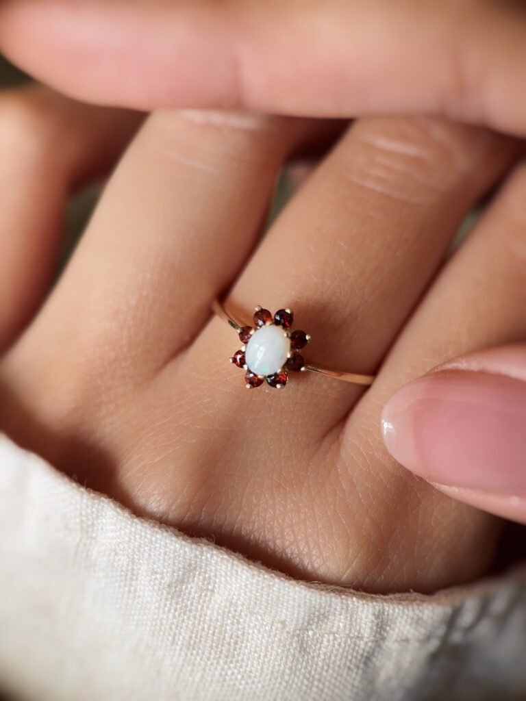 Vintage gold ring with oval opal and red garnets worn on a hand