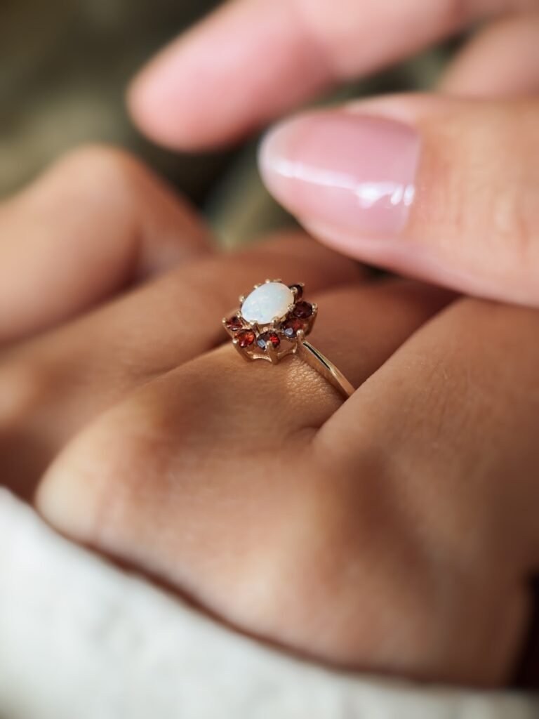 Vintage gold ring with oval opal and red garnets worn on a hand